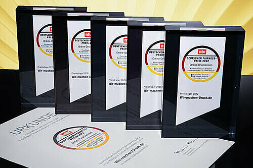 Die fünf Awards für den Deutschen Fairness-Preis, die WirmachenDruck gewonnen hat, in einer Reihe. Unter den Awards liegt eine Urkunde.