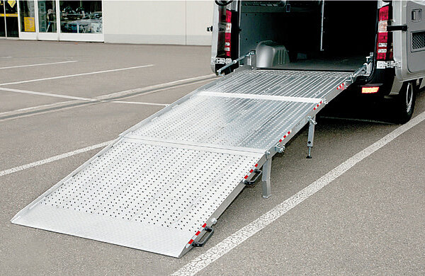 Ein Transporter mit offenen Hecktüren und ausgeklappter Aluminium Verladeschiene vom Typ RRK-Z der Firma Altec steht auf einem Parkplatz.